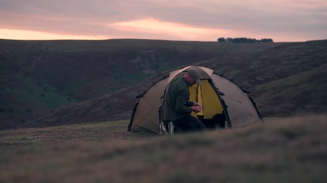 A man doing something inside his wild camping tent in the hills
