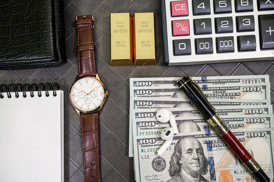 Close up of Men Gold Wristwatch Fine Gold Bars 100 US Dollar Bills and Calculator Desk Frame