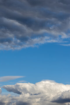 A vertical weather scene displaying a central clear blue sky sandwiched between heavy dark storm clouds at the top and bright white cumulus clouds at the bottom, providing central copy space