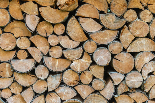 Detailed full frame view of split firewood logs stacked outdoors. The wood grain and bark textures highlight winter energy preparation
