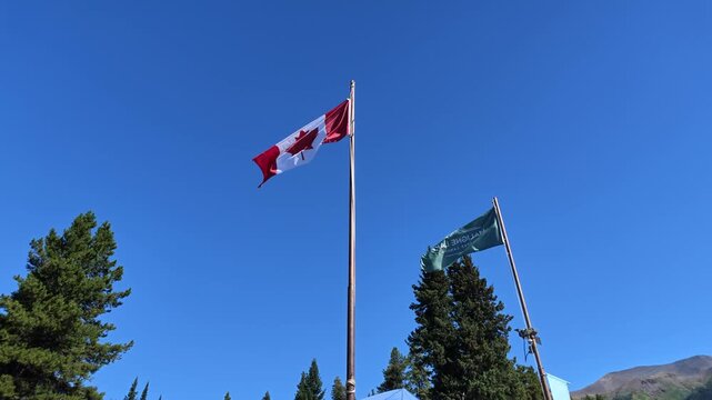 Canada and Jasper National Park flags flutter over evergreen forest and the Rocky Mountains under a blue sky in Maligne Lake, symbolizing national pride and rugged natural beauty in Alberta of Canada