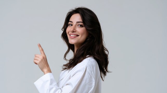 Warm studio portrait of a female healthcare professional, smiling and pointing upward with the index finger, neutral backdrop