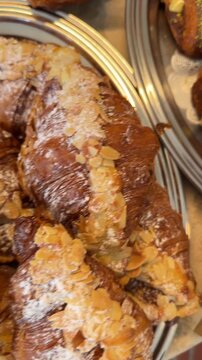 Overhead view of assorted pastries on silver serving trays with oozing pistachio filling, almond topped croissant, and braided knot layers under warm light, textured