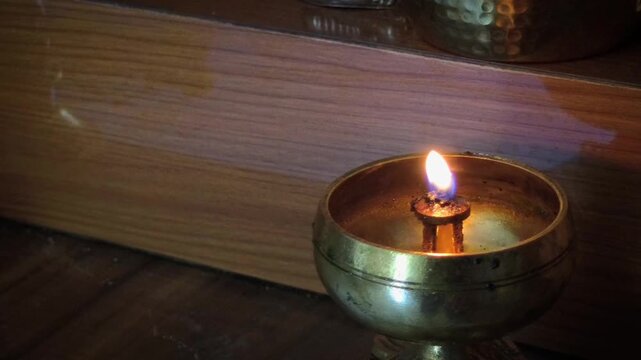 Smooth right-to-left panning video clip of a glowing flame in a traditional brass oil lamp (diya) sitting on a wooden surface. Ideal for spiritual themes, cultural festivals like Diwali, prayer ritual