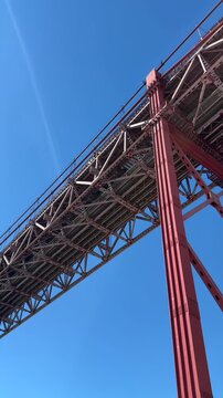 Airplane flying above 25 de Abril Bridge near Doca de Santo Amaro in Lisbon Portugal, low angle view of iconic suspension bridge with commercial aviation crossing the clear blue sky