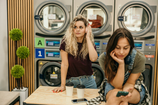 Women waiting in laundromat, checking phone and listening music