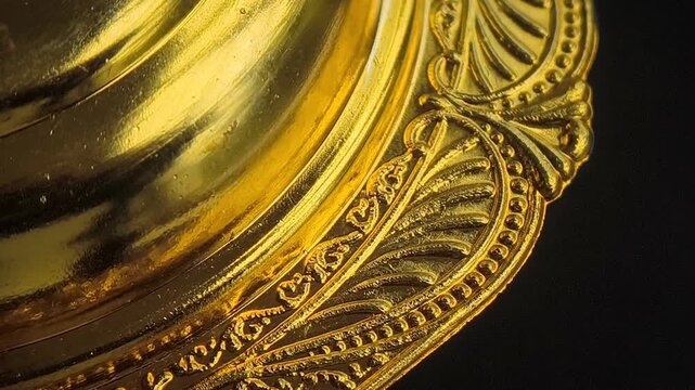 Smooth rotating macro video clip of a luxurious golden metallic object featuring intricate vintage engravings and ornate relief patterns against a dark background. Perfect for luxury backgrounds.