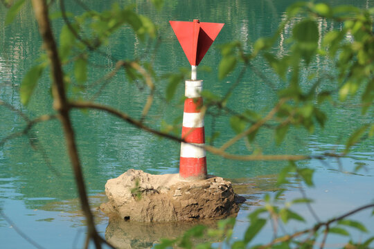 Horizontal composition of a red and white striped river navigation beacon on a stone base in the water in Phong Nha, Vietnam.