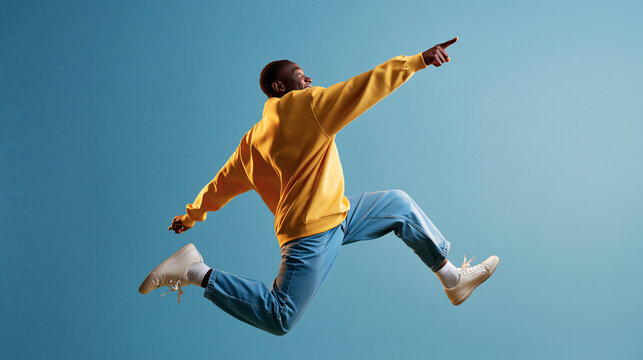 Faceless African American man in a yellow shirt jumping high and pointing aside on a pastel blue background, people lifestyle concept, with copy space