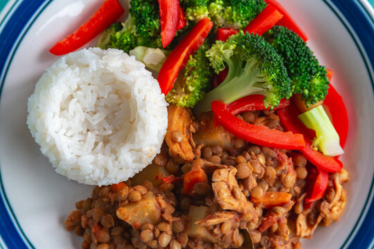 Fresh rice sits beside vibrant vegetables and hearty lentils. Red peppers and broccoli add color to the dish. Chicken pieces blend into the savory lentil mixture