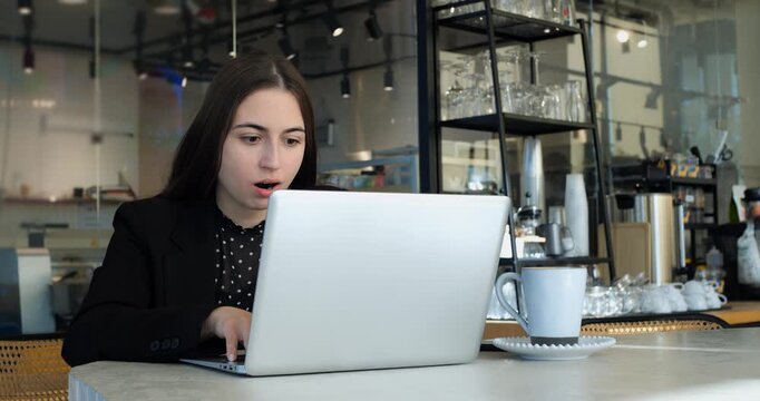 Tired young businesswoman works on laptop during coffee break in modern cafe, yawns repeatedly and closes portable computer to rest from heavy job stress and online workload indoors.
