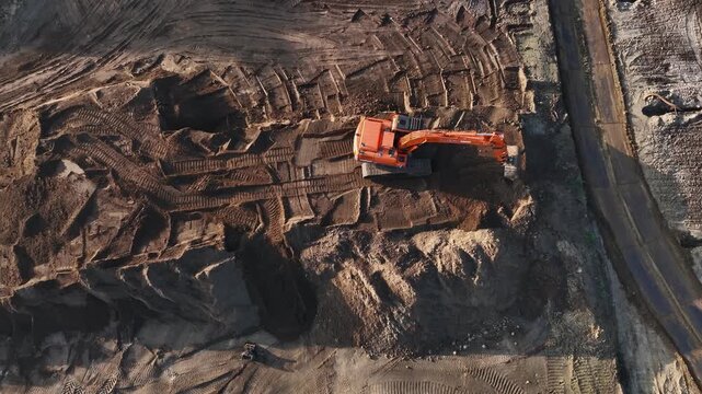 Aerial view of an orange excavator working on a large construction site with deep tire tracks in the soil in Enschede, Overijssel, Netherlands.