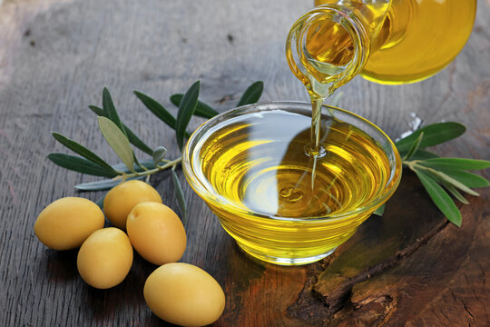 Organic olive oil pouring from a glass carafe into a glass bowl