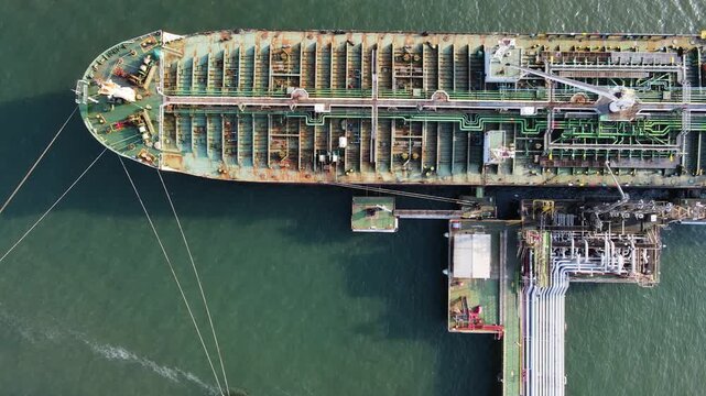 Aerial view of a large tanker ship moored at an industrial terminal with visible piping and mooring lines in Cilacap Regency, Central Java, Indonesia.