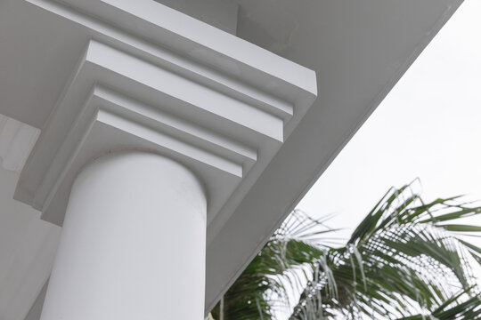A white classical column with crisp molding and clean overhang on a tropical porch, framed by palm leaves. The architectural detail evokes coastal elegance, calm summer vibes