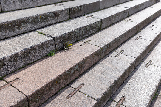 Weathered stone steps with iron anchor fittings and patches of moss and weeds, showing textured granite surfaces, wear and historic urban character ideal for architectural, heritage, and backgrounds