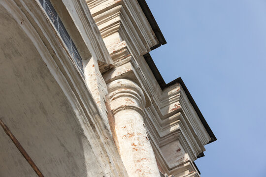 Old church facade featuring weathered stone columns, molded cornices and stucco ornamentation bathed in warm sunlight against a blue sky, emphasizing texture and classical architecture