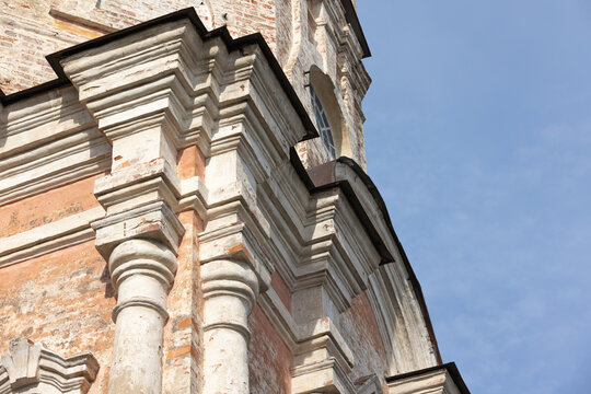 Historic church facade featuring weathered stone columns, molded cornices and stucco ornamentation bathed in warm sunlight against a clear blue sky, emphasizing texture, age and classical architecture