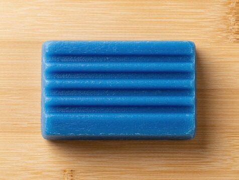 Blue laundry detergent soap bar on light wooden background. Rectangular solid cleaning agent with ridges for manual washing. Single handmade organic soap product for household hygiene, laundry care