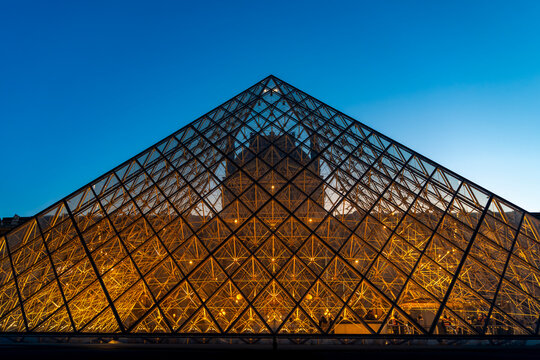 Louvre pyramid featuring geometric glass patterns illuminated at blue hour with a clear sky in paris