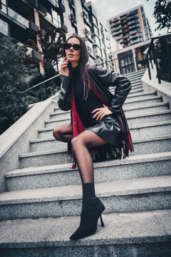 Gorgeous woman in a fashionable leather jacket posing outdoors on modern urban stairs on a sunny day