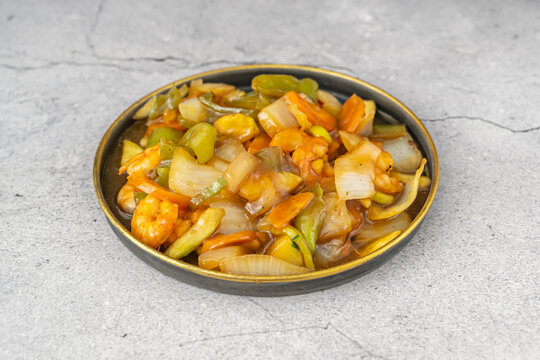 Shrimp and onion chop suey in a gold-rimmed black plate set on a cracked concrete surface