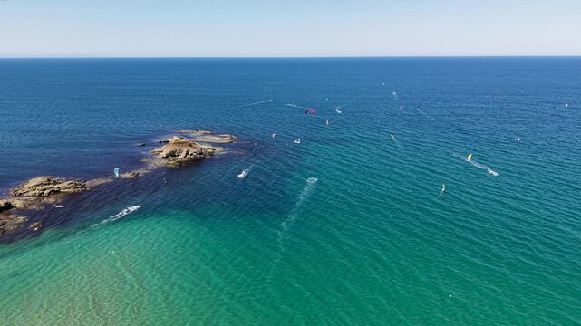 Aerial view of kite surfers gliding across the clear turquoise waters of the Black Sea near the rocky coastline of Lozenets, Burgas, Bulgaria.