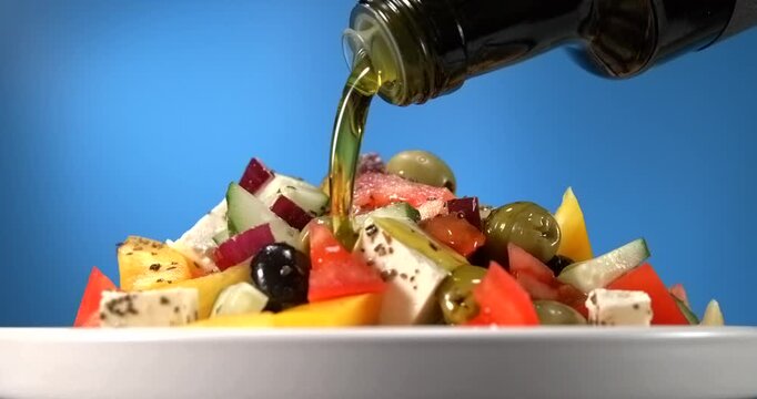 Olive oil pouring onto fresh greek salad with feta cheese olives tomato and cucumber in slow motion