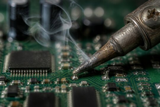 Soldering iron melting solder on circuit board closeup