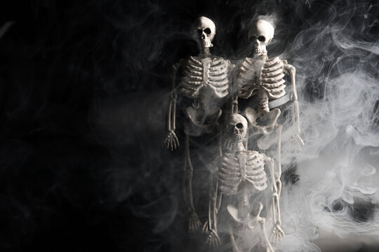 Skeletons emerging from thick white smoke on black background
