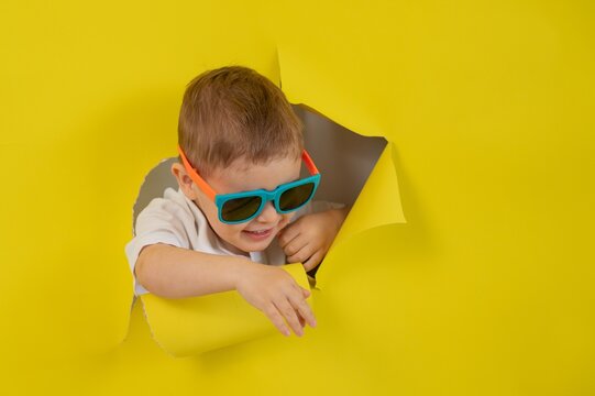Caucasian little boy in sunglasses tearing yellow paper background. 