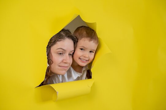 Caucasian little boy and his mother tearing yellow paper background. 