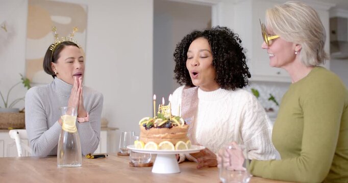 Diverse women friends singing at kitchen table African American woman holding cake blowing candles