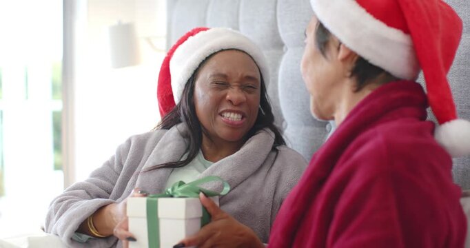 Senior Asian man and African woman laughing, teasing with christmas gift, man reaching