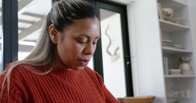African American woman in sweater scanning kitchen bench taking knife slicing yellow pepper to cook