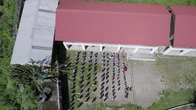 Aerial view of students standing in orderly rows in a school courtyard in front of a building with a red roof in Syapru Besi, Bagmati Province, Nepal.