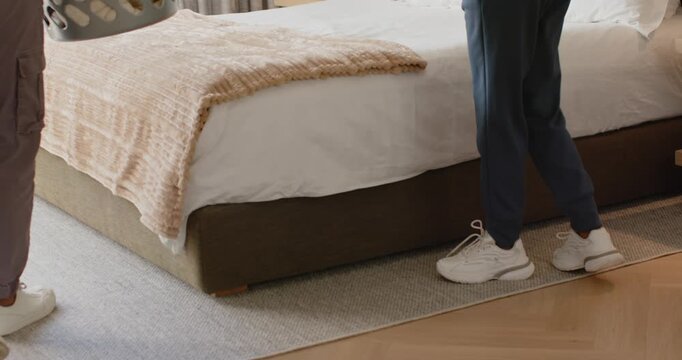 Couple carrying laundry basket, placing on bed at home, sorting clothes to fold