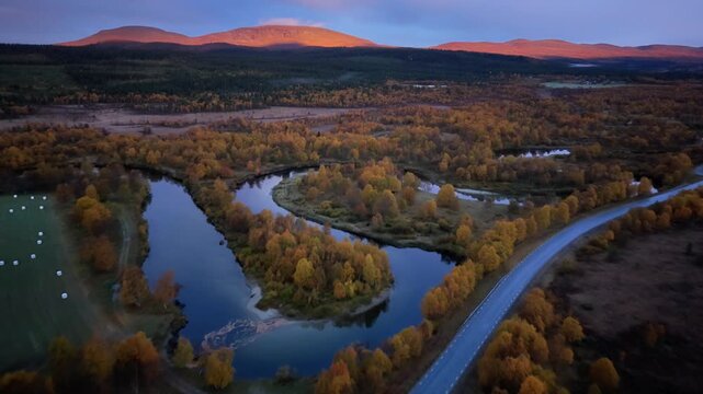 Aerial view of Ljusnan river at sunrise with golden autumn trees and mountains in the background in Funasdalen, Jamtland County, Sweden.