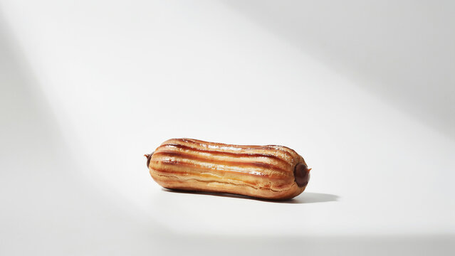 Golden brown eclair pastry with subtle stripes on white background, keywords: eclair, pastry