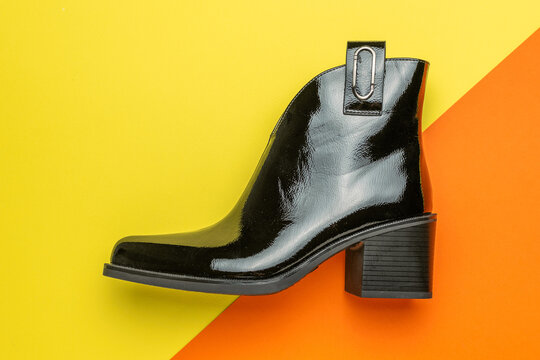 Glossy Black Ankle Boot on Vibrant Yellow and Orange Background - Contemporary Fashion Footwear