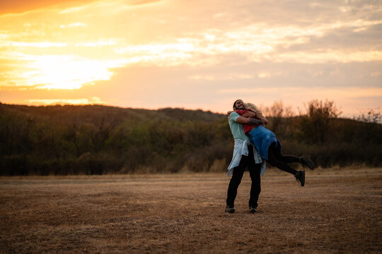 Happy couple hugging spinning in field at sunset