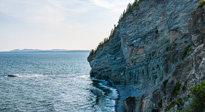 Rocky coastal cliffs overlooking the Gulf of Saint Lawrence in Gasp&eacute;sie, Quebec, Canada, with forested shoreline and calm blue water.