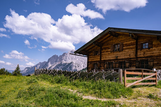 Uriges Holz-Almhaus mit traditionellem Schr&auml;gzaun vor den Berchtesgadener Alpen.
