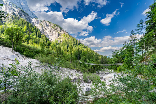 Klausbachtal-H&auml;ngebr&uuml;cke &uuml;ber ein helles Ger&ouml;llfeld vor steilen Bergw&auml;ldern und Felsw&auml;nden.