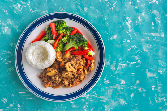 Freshly plated dish of rice, vegetables, and meat. Bright turquoise background adds bold contrast. Healthy meal looks appetizing and balanced. Top-down view highlights dish's appealing composition