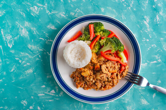 Bright plate holds steamed rice, broccoli, and seasoned meat. Red peppers add color to the vibrant meal. Fork rests beside the dish, ready for use