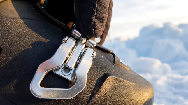 Close up of metallic ski boot buckle on black footwear against snowy mountain landscape during resort preparation, outdoor winter sports equipment detail