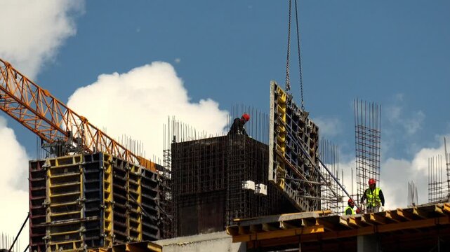 Tyumen, Russia - September 20, 2026: Building team installs concrete forms with crane assistance on busy construction site. Skilled laborers maneuver structural parts on elevated architecture.