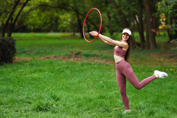Athletic young woman exercising with hula hoop in park, space for text © New Africa