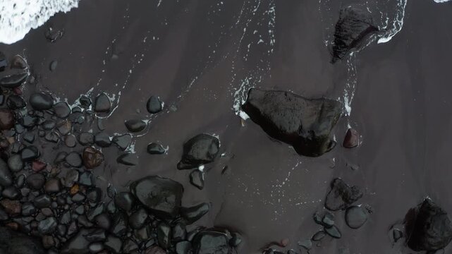 4K contrasty footage of bright foamy white waves rolling onto sandy black beach with black stones in Madeira, Portugal